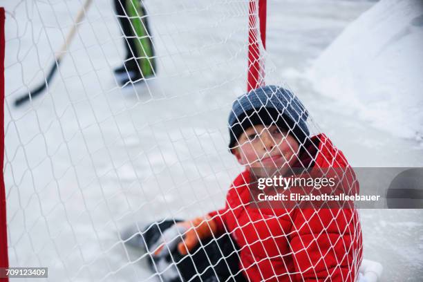 boy sitting inside hockey goal - hockey kids stock-fotos und bilder