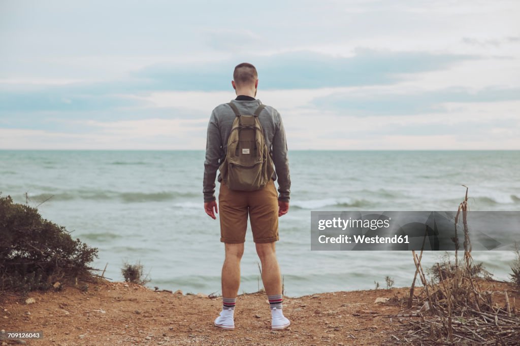 Back view of young man with backpack looking to the sea