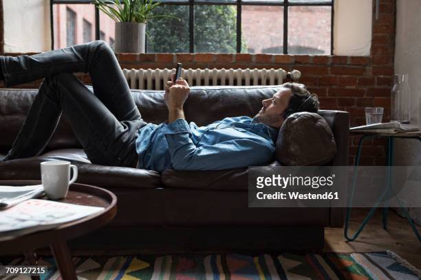 man lying on couch, using smart phone - man sofa stock pictures, royalty-free photos & images