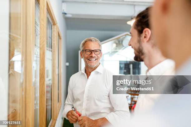 smiling businessman looking at colleagues in office - business man confident stock-fotos und bilder