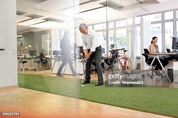 businessman playing golf in office - practicing stockfoto's en -beelden