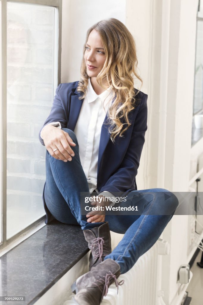 Businesswoman sitting on window sill of her office