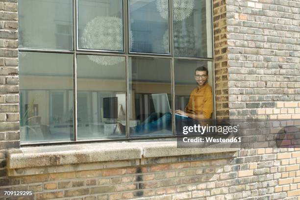 young professional at the window looking confident, using laptop - window sill stock pictures, royalty-free photos & images