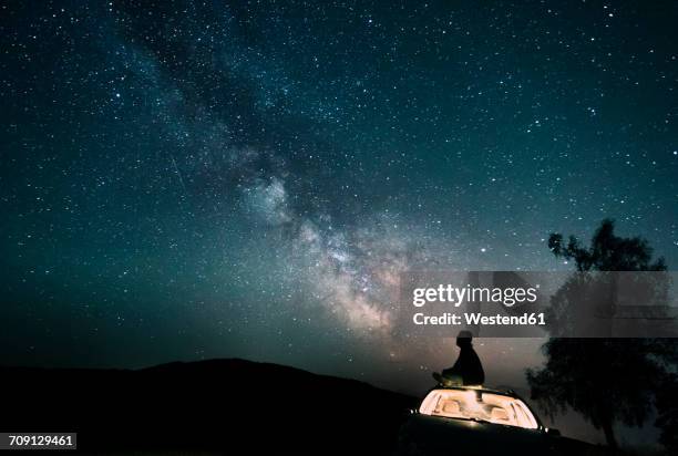 austria, mondsee, silhouette of man sitting on car roof under starry sky - stars sky stockfoto's en -beelden