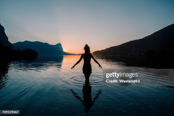 austria, mondsee, lake mondsee, silhouette of woman standing in water at sunset - eskapismus stock-fotos und bilder