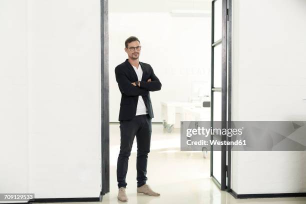 young businessman standing in his office with arms crossed - business man standing stock-fotos und bilder