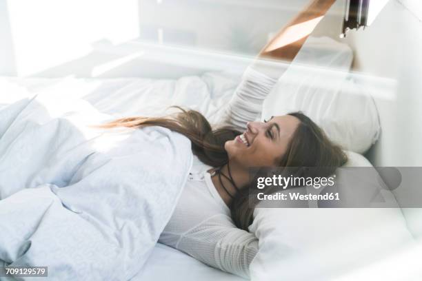 smiling young woman lying in bed - woman waking up happy stock pictures, royalty-free photos & images