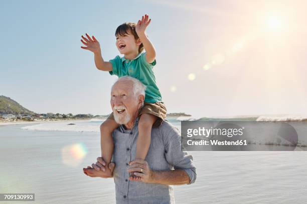 happy senior man with grandson on his shoulders on the beach - grandfather stock pictures, royalty-free photos & images