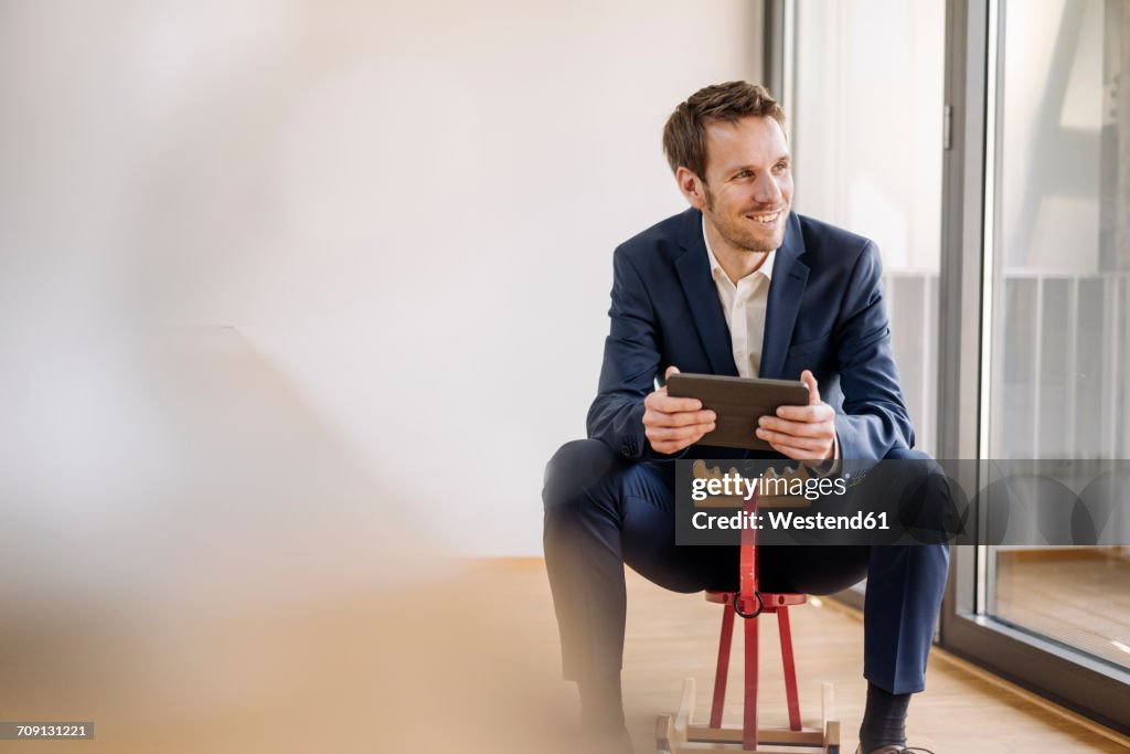 Smiling businessman sitting on rocking horse with tablet