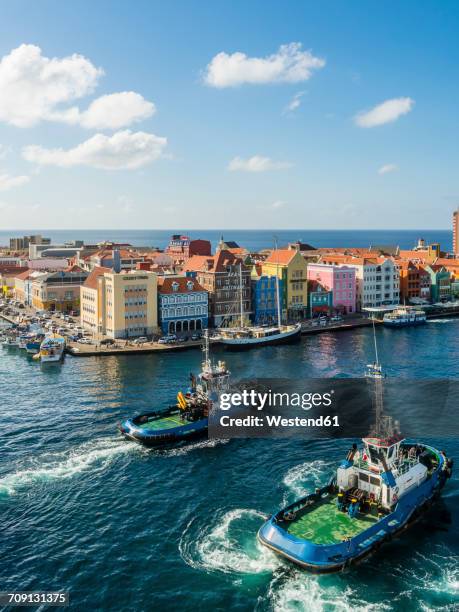 curacao, willemstad, punda, tugboats and colorful houses at waterfront promenade - curaçao stockfoto's en -beelden