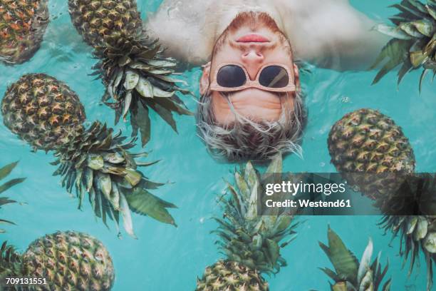 young man in swiming pool surrounded by pineapples - crazy pool foto e immagini stock