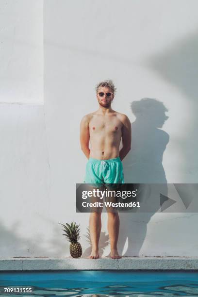 young man standing at the poolside next to pineapple - swimwear ストックフォトと画像