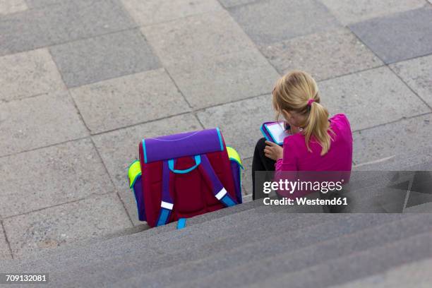 back view of little girl with school bag sitting on stairs doing homework - summer camp stock-fotos und bilder