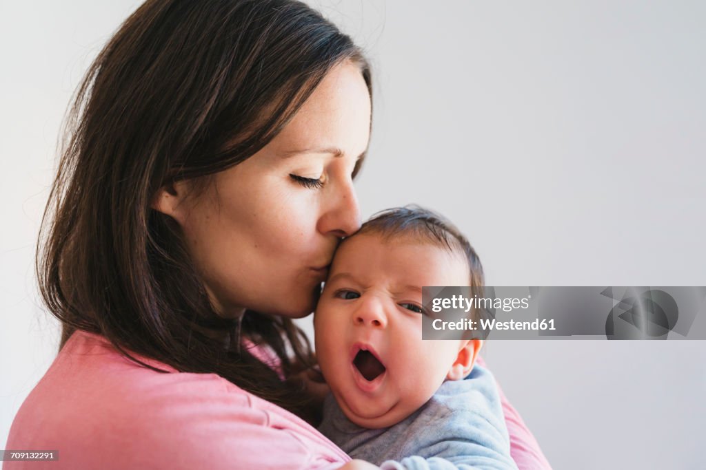Woman holding and kissing a baby yawning