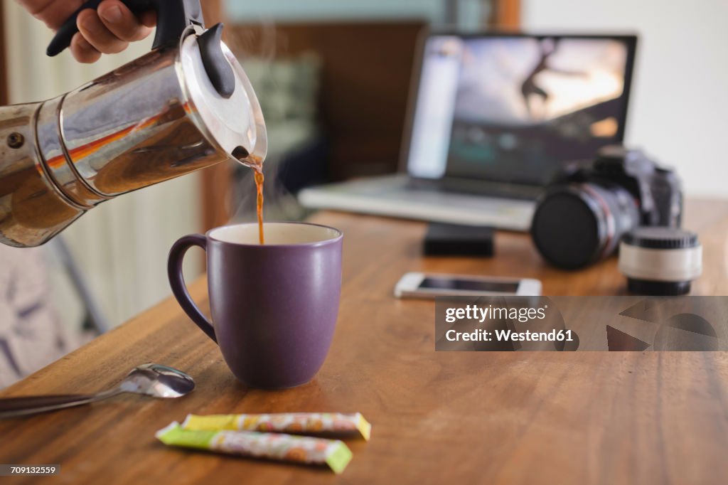 Photographer pouring coffee into cup at desk at home