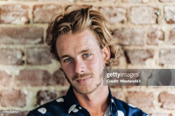 portrait of confident blond man at brick wall - young man blue eyes stock pictures, royalty-free photos & images