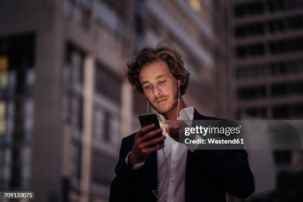 businessman in the city at dusk using cell phone - young man listening to music on smart phone outdoors stockfoto's en -beelden