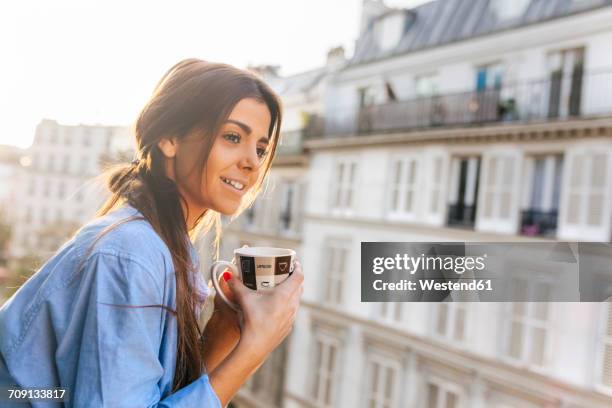 young woman standing on balcony, holding cup of coffee - paris balcony stock pictures, royalty-free photos & images