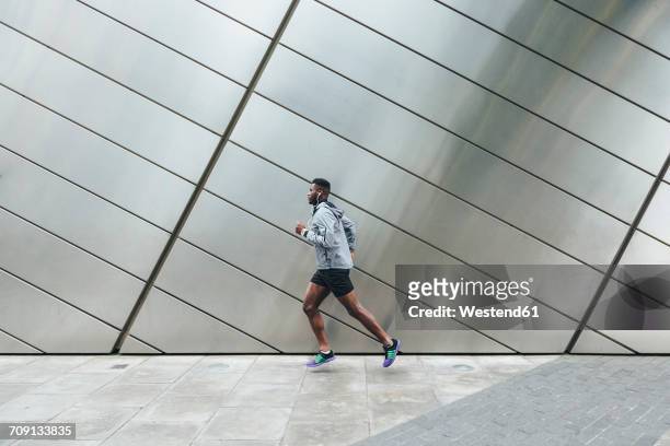 young man running along building front - man running city fotografías e imágenes de stock