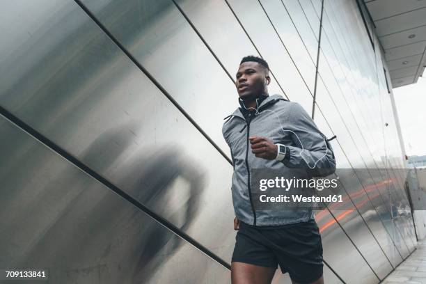 young man running along building front - sportswear man stock pictures, royalty-free photos & images