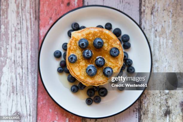 dish with pile of pancakes and blueberries with maple sirup - blueberry pancakes stock pictures, royalty-free photos & images