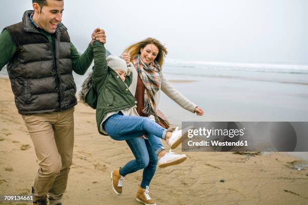 happy parents lifting up daughter on the beach in winter - beach winter stock pictures, royalty-free photos & images