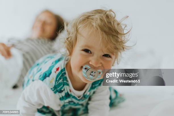 portrait of happy little girl with mother in bed - pacifier stockfoto's en -beelden