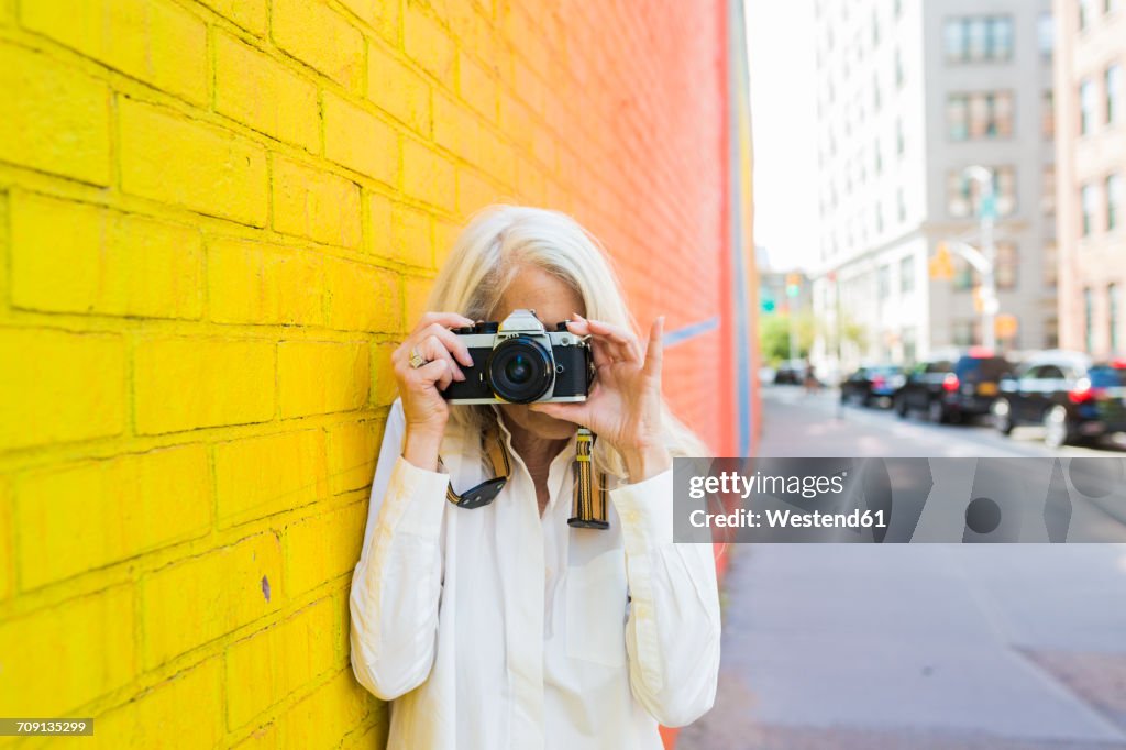 Mature woman leaning against wall taking picture with camera