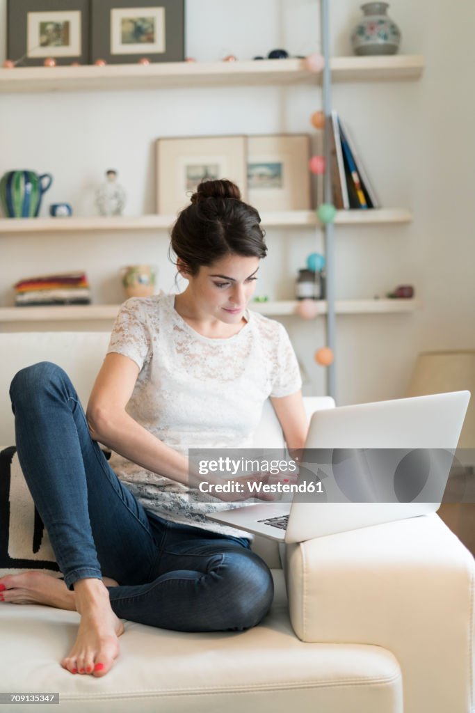 Woman sitting on couch at home using laptop