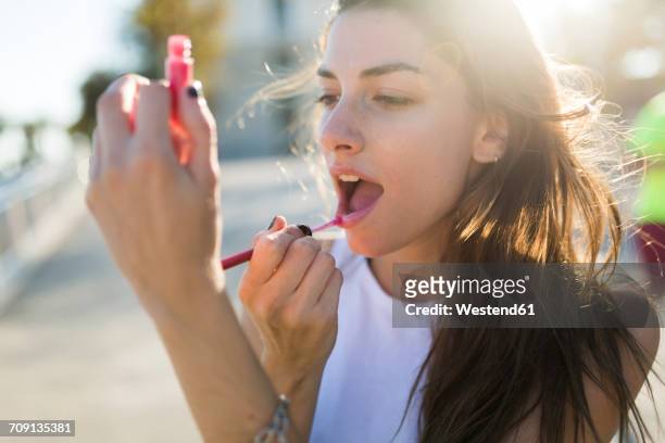 portrait of young woman applying lip gloss - lipgloss stockfoto's en -beelden
