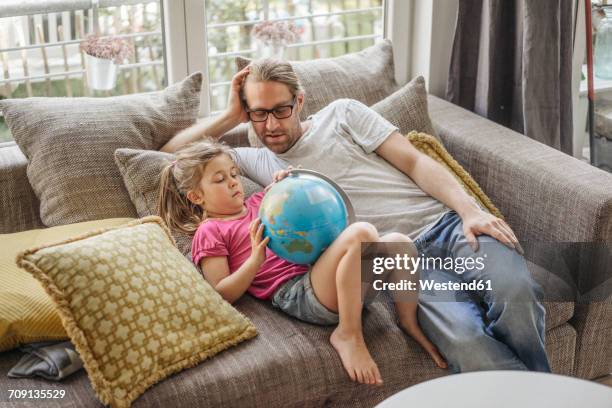 father and daughter lying with globe on sofa - genderblend stock-fotos und bilder