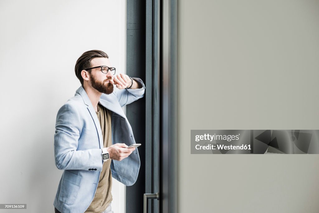 Young businessman standing in office, using smart phone