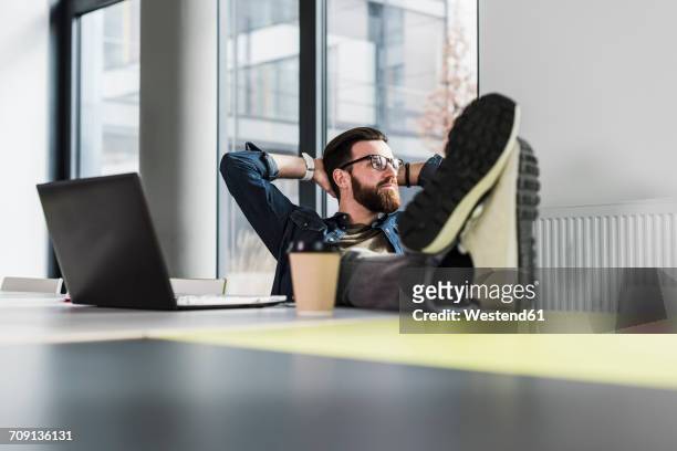 young casual businessman sitting in office with feet up and a cup of coffee - feet up stock pictures, royalty-free photos & images