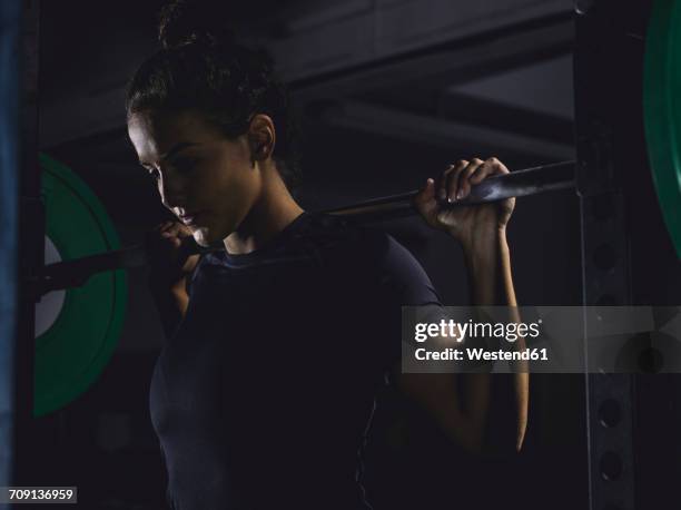 young woman lifting barbell in power rack - ambient light stock pictures, royalty-free photos & images