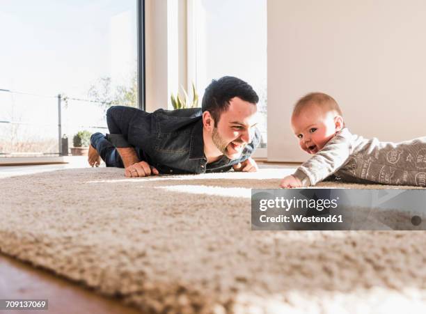 father and baby son playing crawling on carpet - gatear fotografías e imágenes de stock