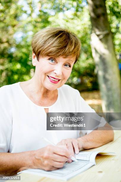 portrait of smiling senior woman doing a crossword puzzle outdoors - teaser stock pictures, royalty-free photos & images