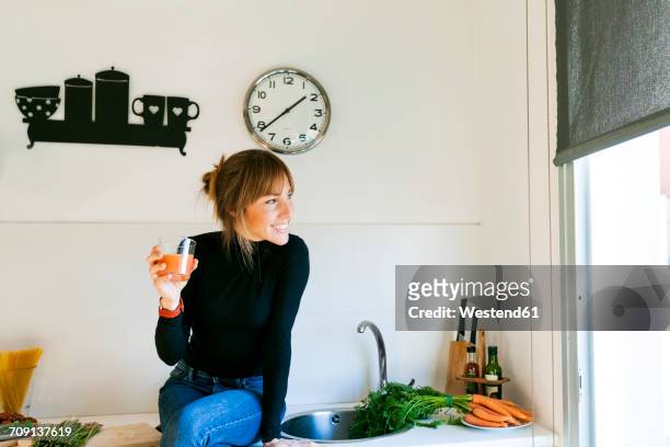 young woman drinking fresh grapefruit juice in her kitchen - wandklok stockfoto's en -beelden