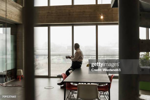 senior manager in office holding cup of coffee, looking serious - oberteil stock-fotos und bilder