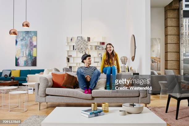 couple in modern furniture store sitting on couch, laughing - sofa stock-fotos und bilder