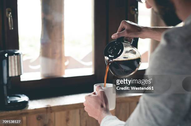 young man pouring coffee into cup at home - fülle stock-fotos und bilder