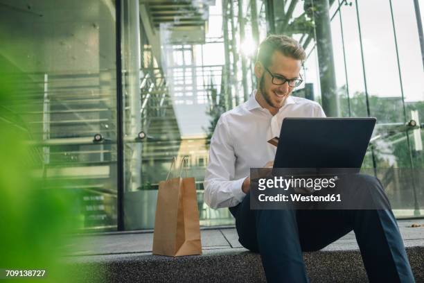 smiling businessman holding credit card and using laptop in lobby - business man sitting banking ストックフォトと画像