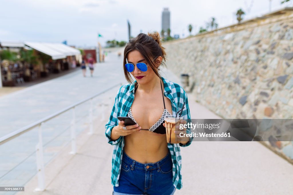 Young woman at the beach with cup of coffee and smart phone