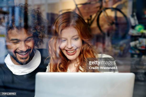 happy young couple using laptop behind windowpane - cafe laptop junge frau stock-fotos und bilder