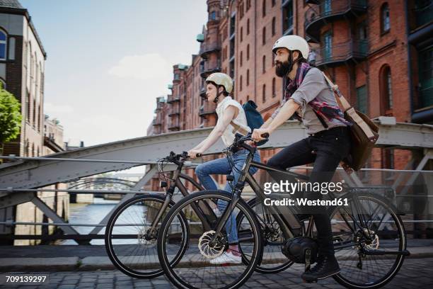 germany, hamburg, couple riding electric bicycles at old warehouse district - hamburg stock-fotos und bilder