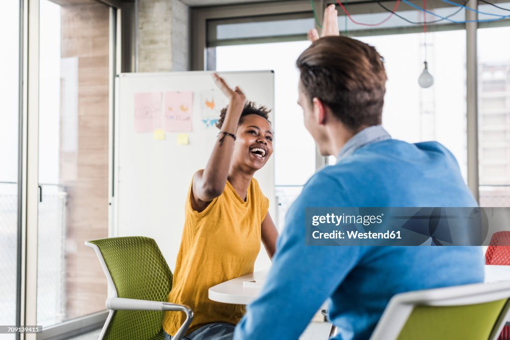 Happy young woman high fiving with colleague in office