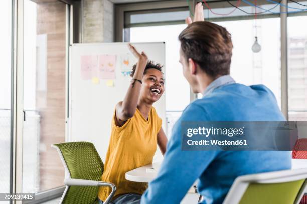 happy young woman high fiving with colleague in office - choque de manos en el aire fotografías e imágenes de stock