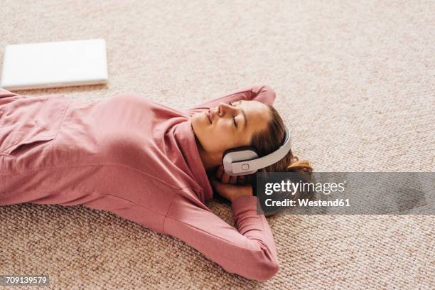 woman lying on carpet wearing headphones - music home stock-fotos und bilder