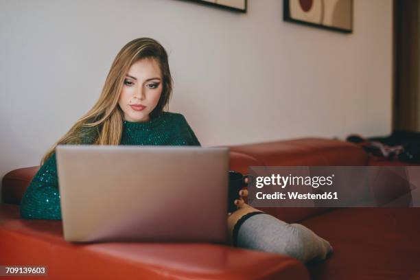 young woman sitting on the couch with cup of coffee using laptop - mole skin notebook stock pictures, royalty-free photos & images