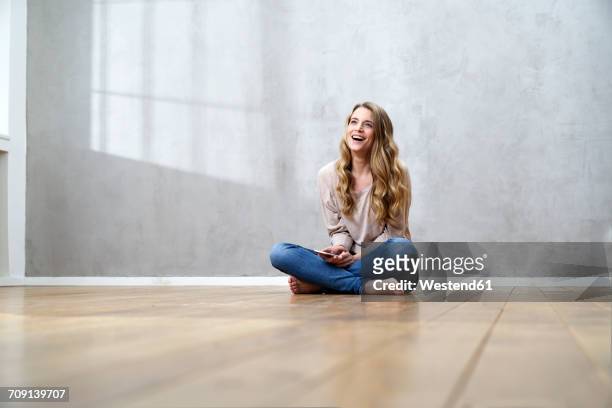 laughing blond woman sitting on the floor with cell phone - cross legged stock pictures, royalty-free photos & images
