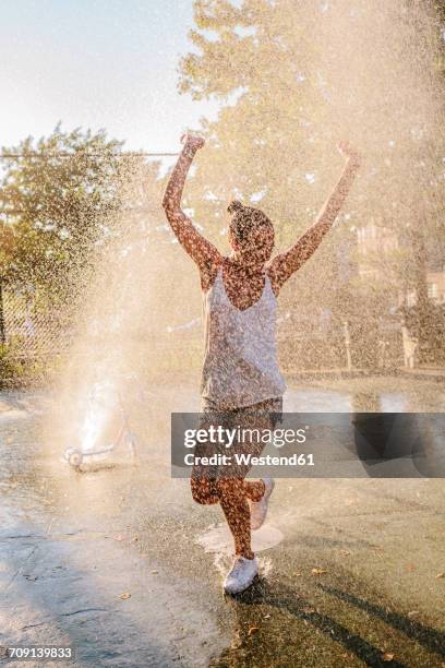 young woman jumping water jet of a fountain - drinkwaterfontein stockfoto's en -beelden